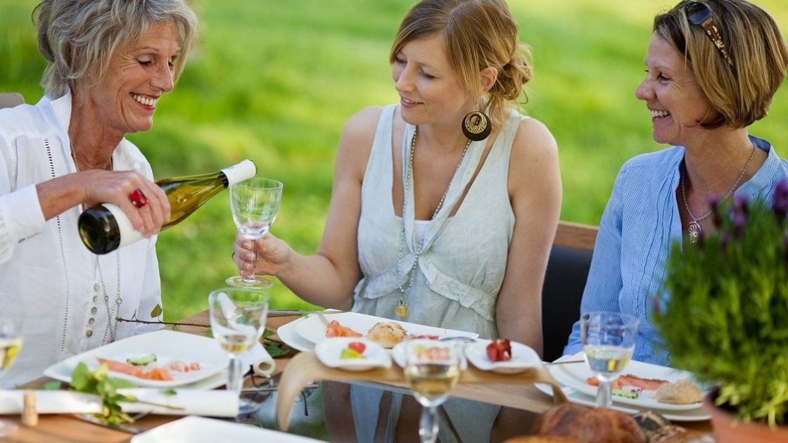 Senior woman pouring wine in glass for daughter at dining table in lawn